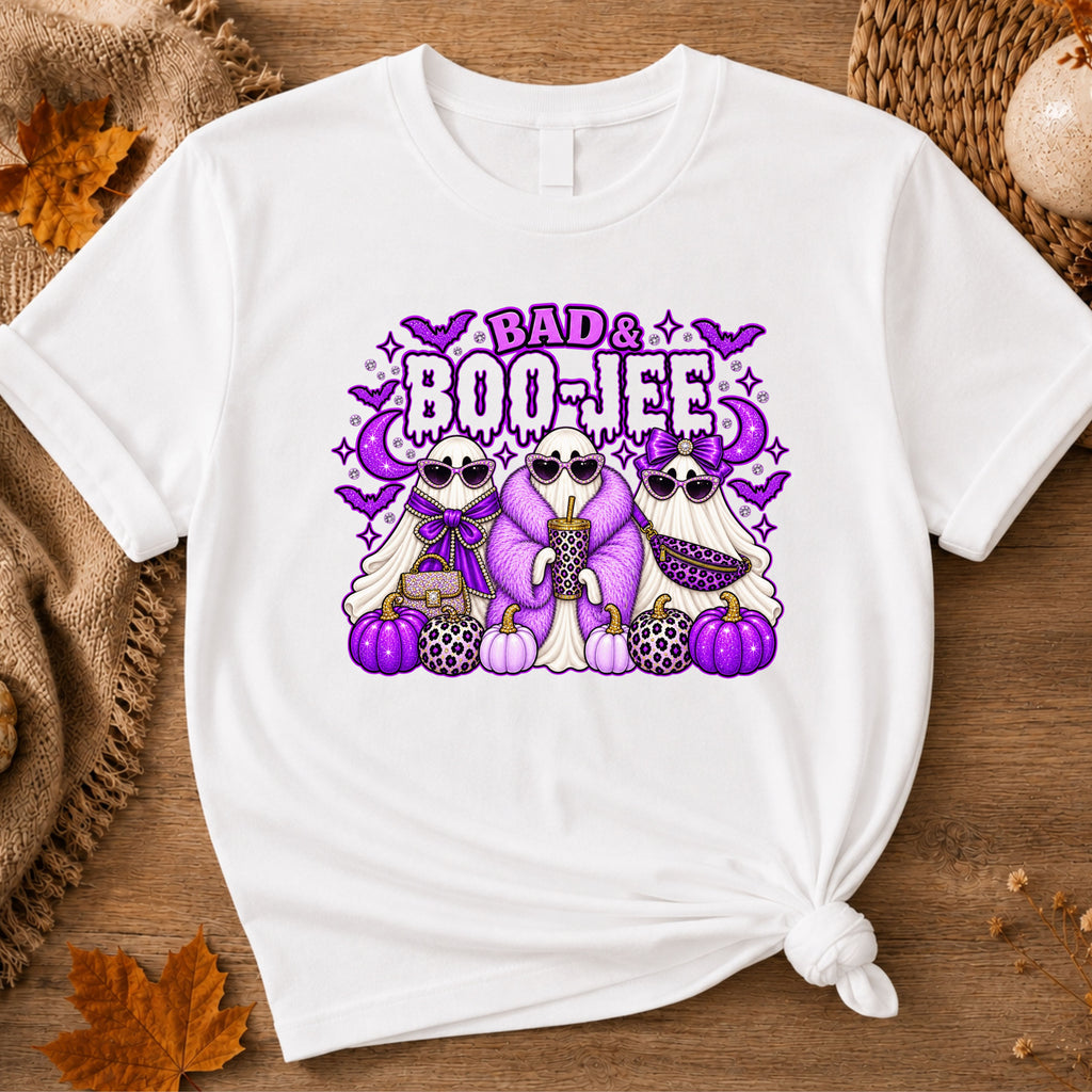 A white short-sleeve t-shirt with a graphic print of three cartoon ghosts wearing sunglasses and leopard-print clothing, standing in front of purple pumpkins and the text 'BAD BOO-JEE'.
