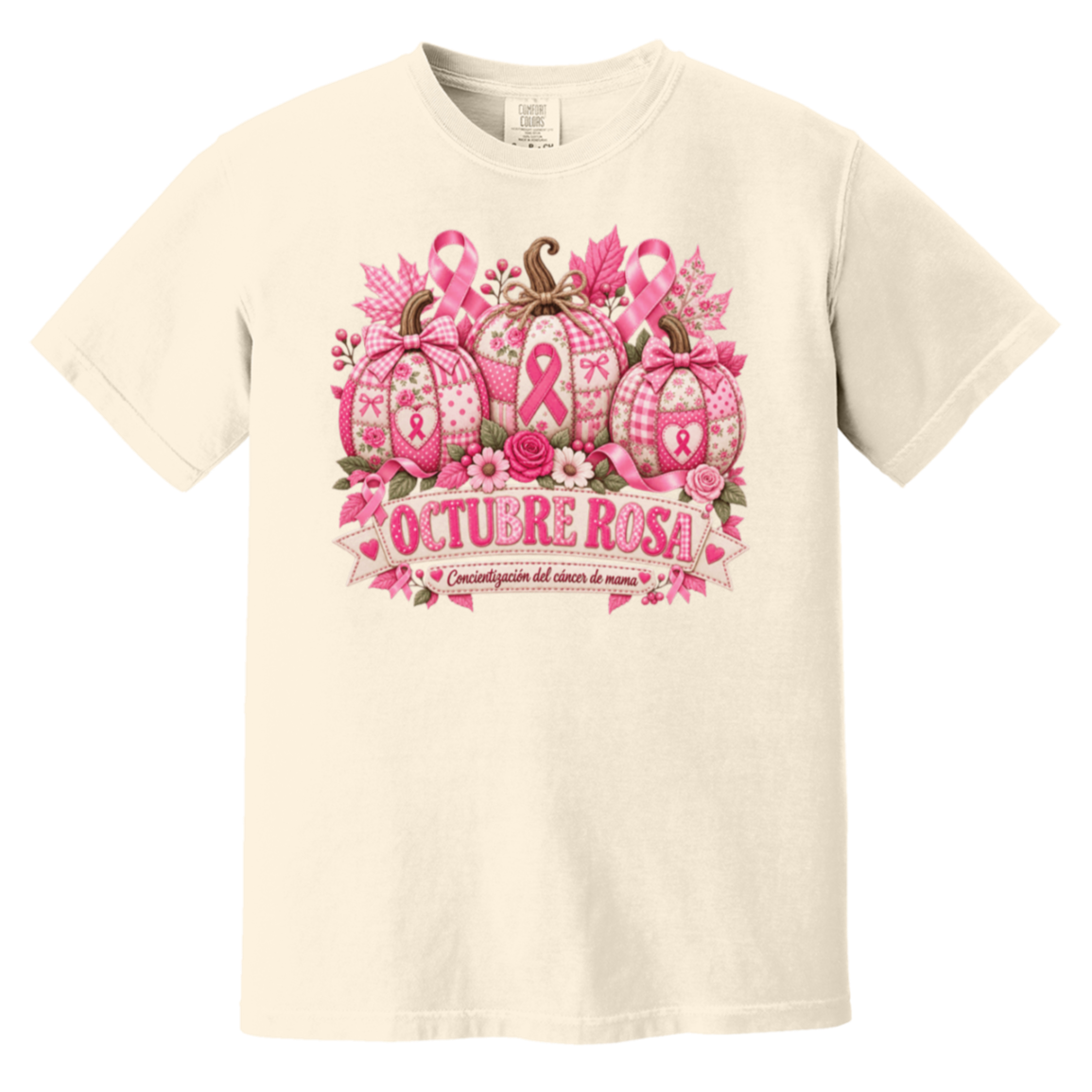 Beige short-sleeve graphic T-shirt laid flat on a rustic wood surface with autumn leaves and woven textiles around it. The shirt features a large pink breast-cancer awareness design with three patterned pumpkins, pink ribbons, flowers, and a banner reading 'OCTUBRE ROSA' with smaller Spanish text saying “concientizacion del cancer de mama”