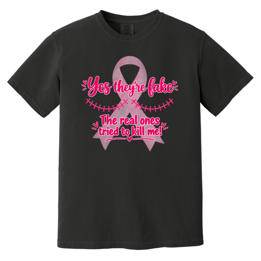 A black short-sleeve t-shirt with a pink graphic on the front. The graphic features a pink ribbon and the text 'Yes they're fake' and 'The real ones tried to kill me!' in pink lettering.