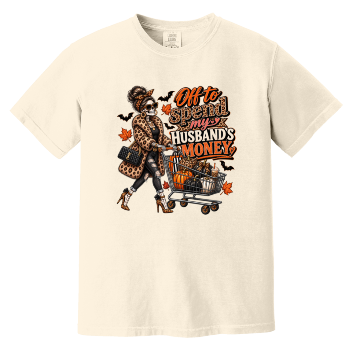 A cream white tshirt featuring a skeleton wearing a leopard print fur coat, pushing a shopping cart full of pumpkins with the text ‘off to spend my husbands money’ 