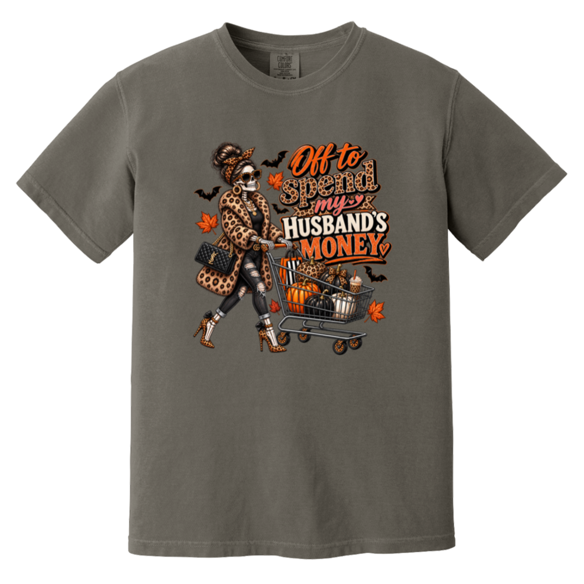A dark gray tshirt featuring a skeleton wearing a leopard print fur coat, pushing a shopping cart full of pumpkins with the text ‘off to spend my husbands money’ 