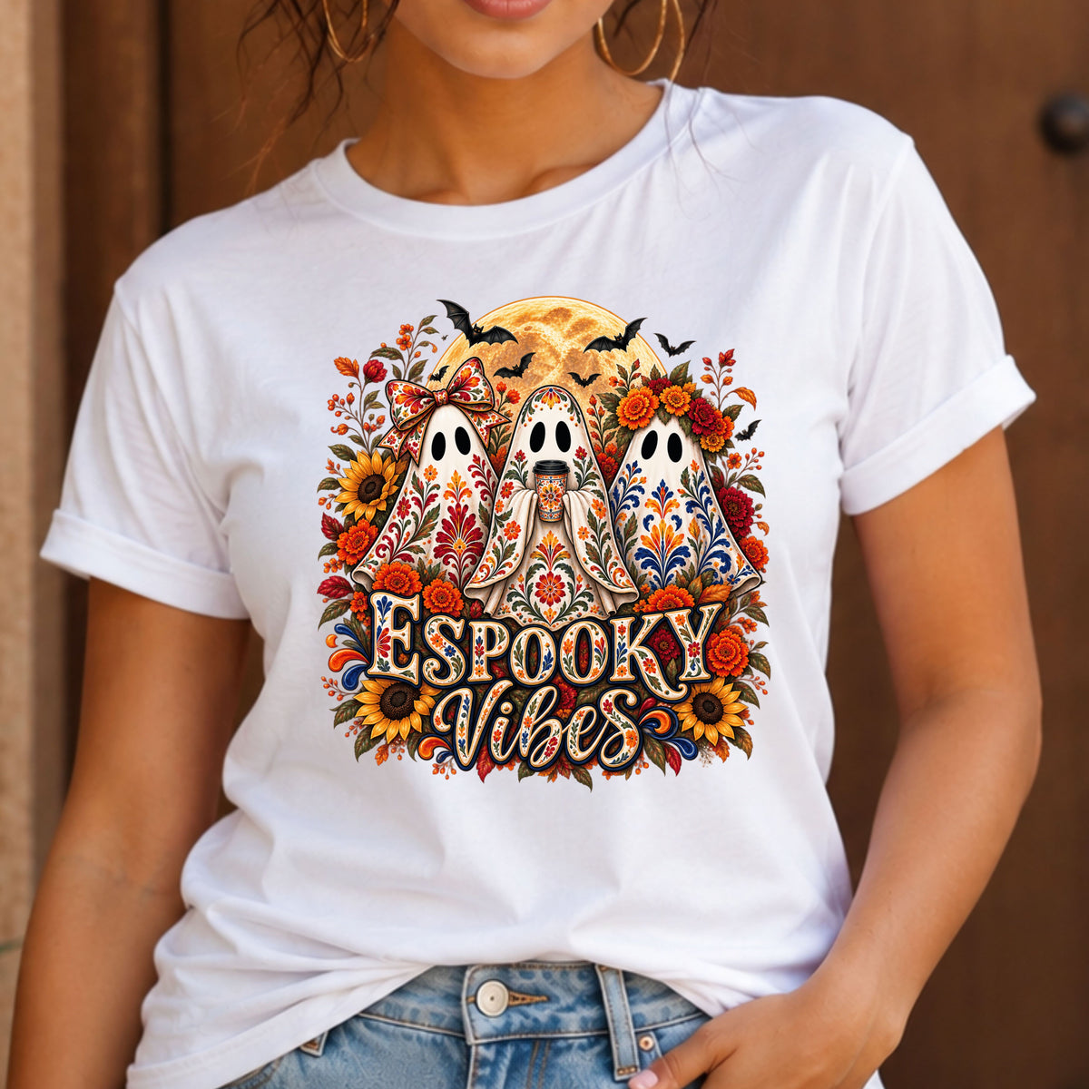 A woman wearing a white short-sleeve graphic T-shirt with a colorful Halloween design featuring three ghosts, flowers, sunflowers, bats, and the text 'Espooky Vibes'.
