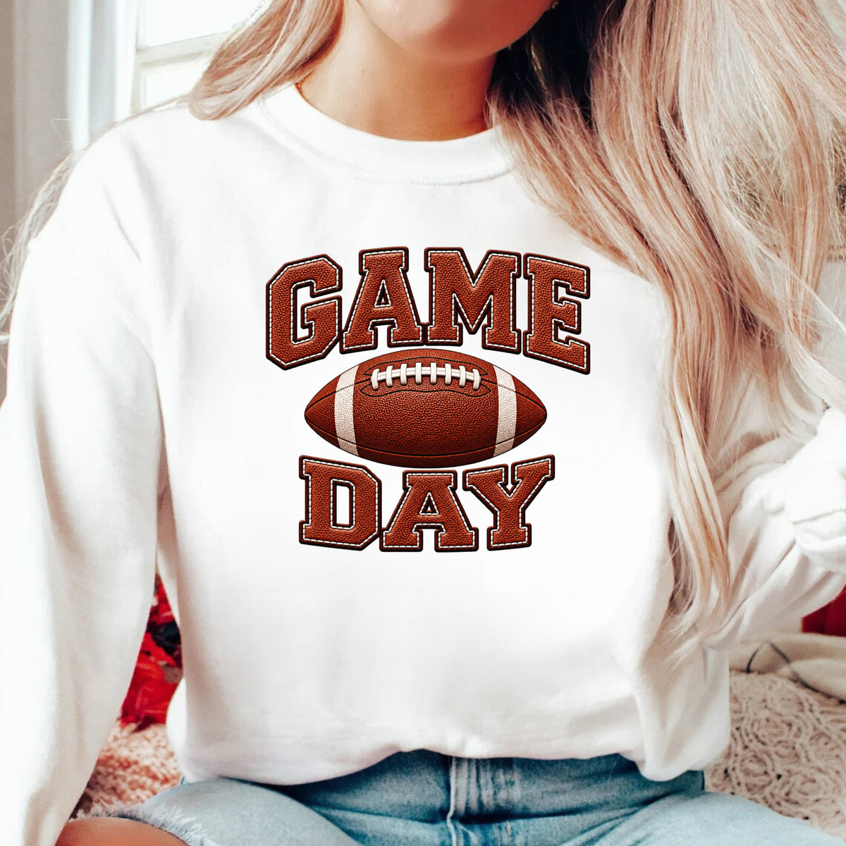 A woman wearing a white crewneck sweatshirt with a brown and red 'GAME DAY' football graphic