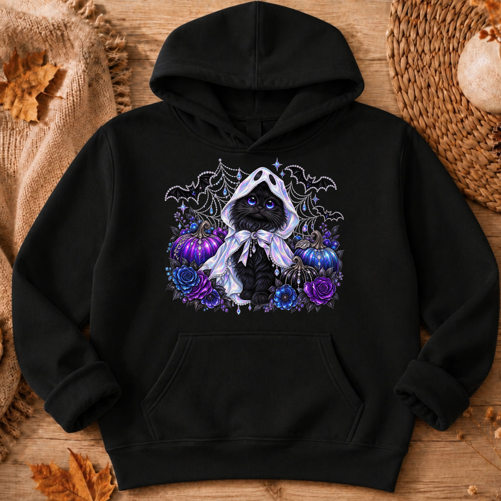 A black pullover hoodie laid flat on a rustic wood surface with autumn-themed props. The front has a large graphic of a black cat wearing a white hood, surrounded by purple and blue flowers, pumpkins, bats, and spiderwebs.