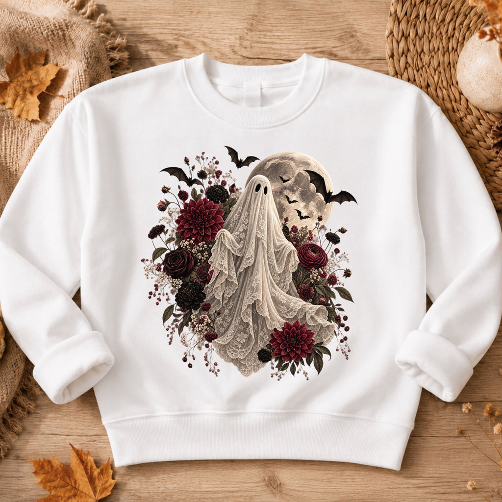 A white crewneck sweatshirt laid flat on a rustic wooden surface, featuring a gothic-style graphic of a ghostly figure draped in lace, surrounded by dark red and black flowers, bats, and a full moon.