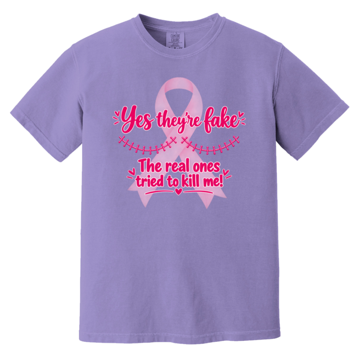 Lavender short-sleeve t-shirt with a pink graphic on the front. The graphic features a pink ribbon and the text 'Yes they're fake' and 'The real ones tried to kill me!' in pink lettering.