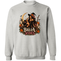 Light gray crewneck sweatshirt with a large graphic print on the front. The graphic features a witch in a black hat sitting on a broomstick next to a black cat, surrounded by orange flowers and the text 'BRUJA VIBES'.