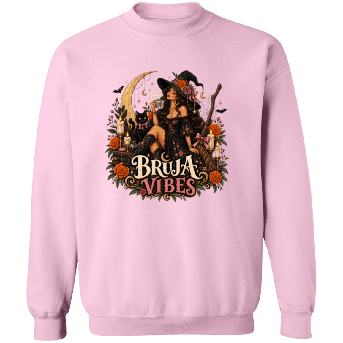 A light pink crewneck sweatshirt with a large graphic print on the front. The graphic features a witch in a black hat sitting on a broomstick next to a black cat, surrounded by orange flowers and the text 'BRUJA VIBES'.