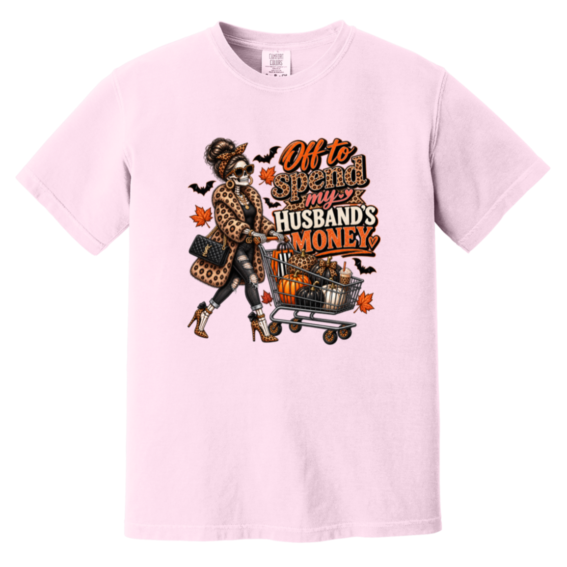 A light pink tshirt featuring a skeleton wearing a leopard print fur coat, pushing a shopping cart full of pumpkins with the text ‘off to spend my husbands money’ 