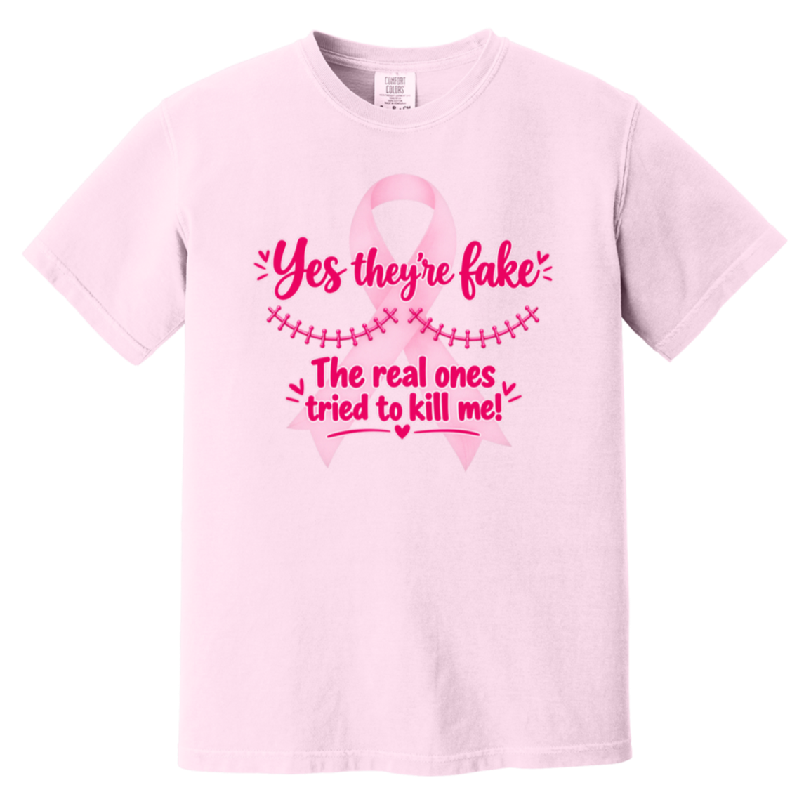 Light pink short-sleeve t-shirt with a pink graphic on the front. The graphic features a pink ribbon and the text 'Yes they're fake' and 'The real ones tried to kill me!' in pink lettering.