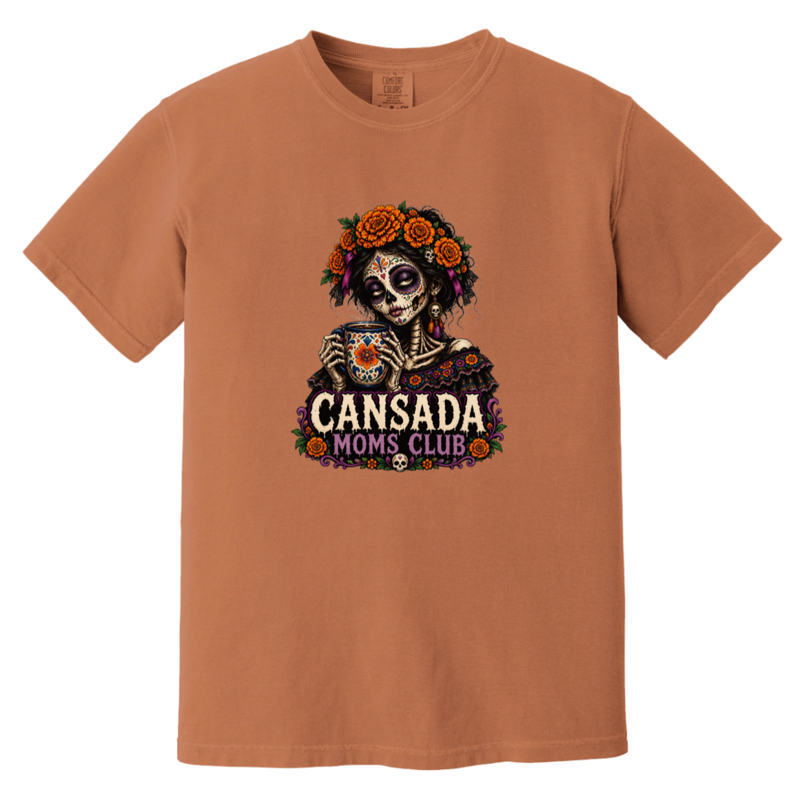 A rust-orange crewneck t-shirt featuring a Day of the Dead sugar skull graphic with orange roses, a teacup, and the text 'CANSADA MOMS, CLUB'.
