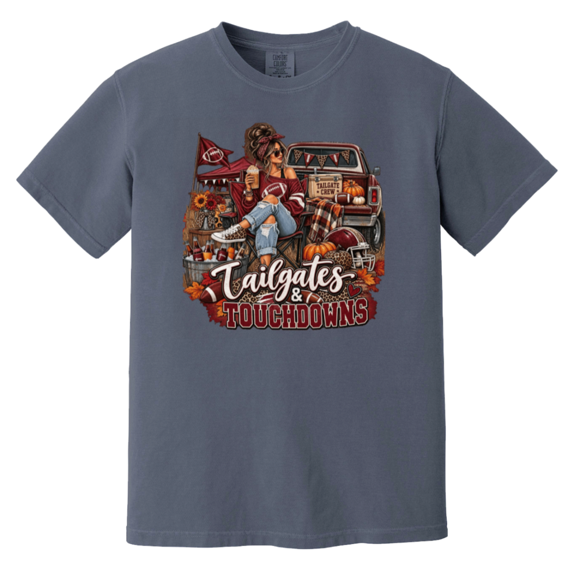 Slate blue graphic T-shirt with a detailed autumn football scene printed on the front, including a truck, pumpkins, sunflowers, and the text 'Tailgates & Touchdowns'.