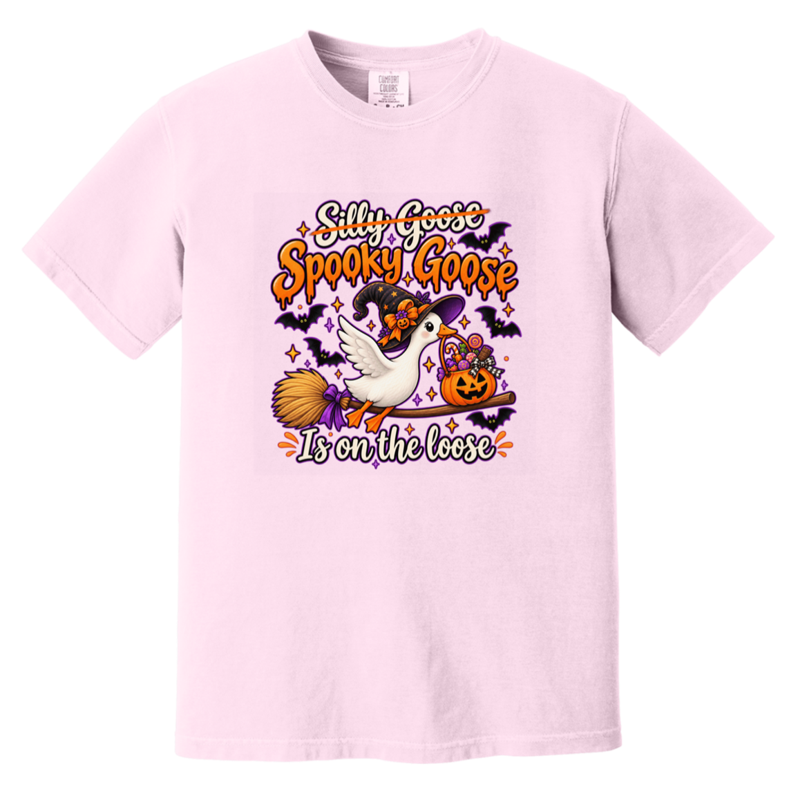 A light pink short-sleeve crewneck t-shirt featuring a colorful Halloween graphic on the chest. The graphic shows a white goose with a witch hat riding a broomstick next to a jack-o'-lantern pumpkin, with the text 'Silly Goose Spooky Goose Is on the loose' in orange, purple, and white lettering.