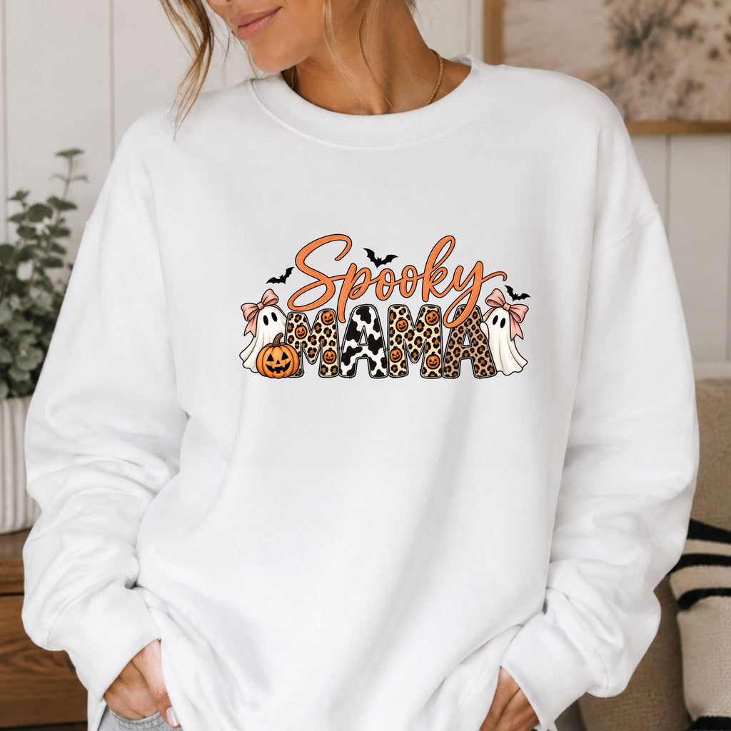 A woman wearing a white crewneck sweatshirt with a 'Spooky Mama' graphic featuring Halloween-themed characters and patterns.