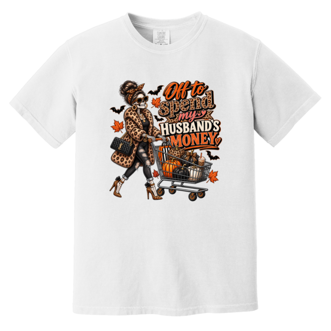 A white tshirt featuring a skeleton wearing a leopard print fur coat, pushing a shopping cart full of pumpkins with the text ‘off to spend my husbands money’ 