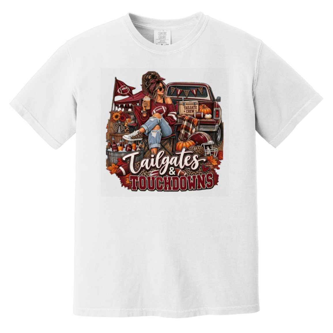 White graphic T-shirt with a detailed autumn football scene printed on the front, including a truck, pumpkins, sunflowers, and the text 'Tailgates & Touchdowns'.