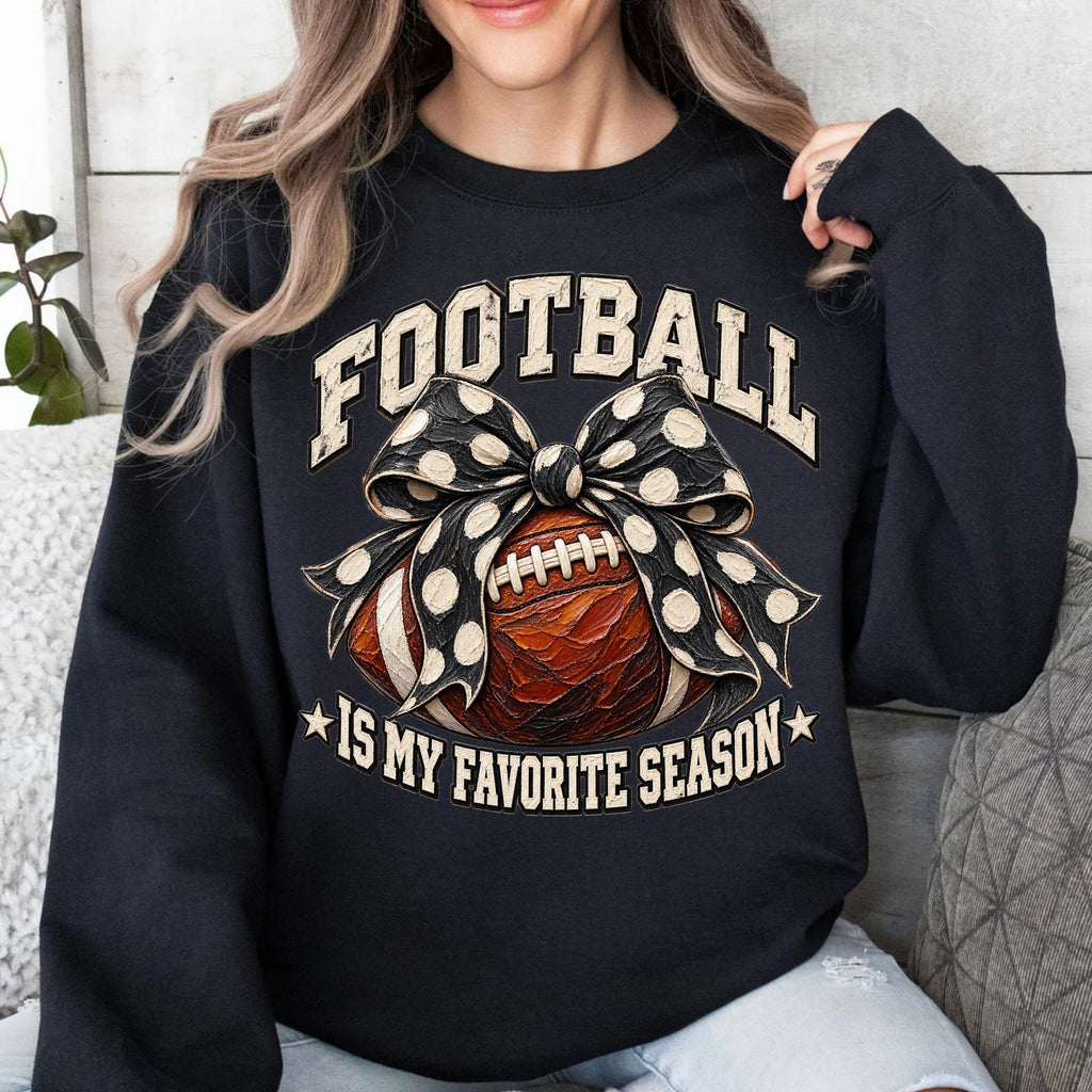 A woman wearing a black crewneck sweatshirt with a graphic that reads 'FOOTBALL IS MY FAVORITE SEASON' around an illustration of a football and a polka-dot bow.