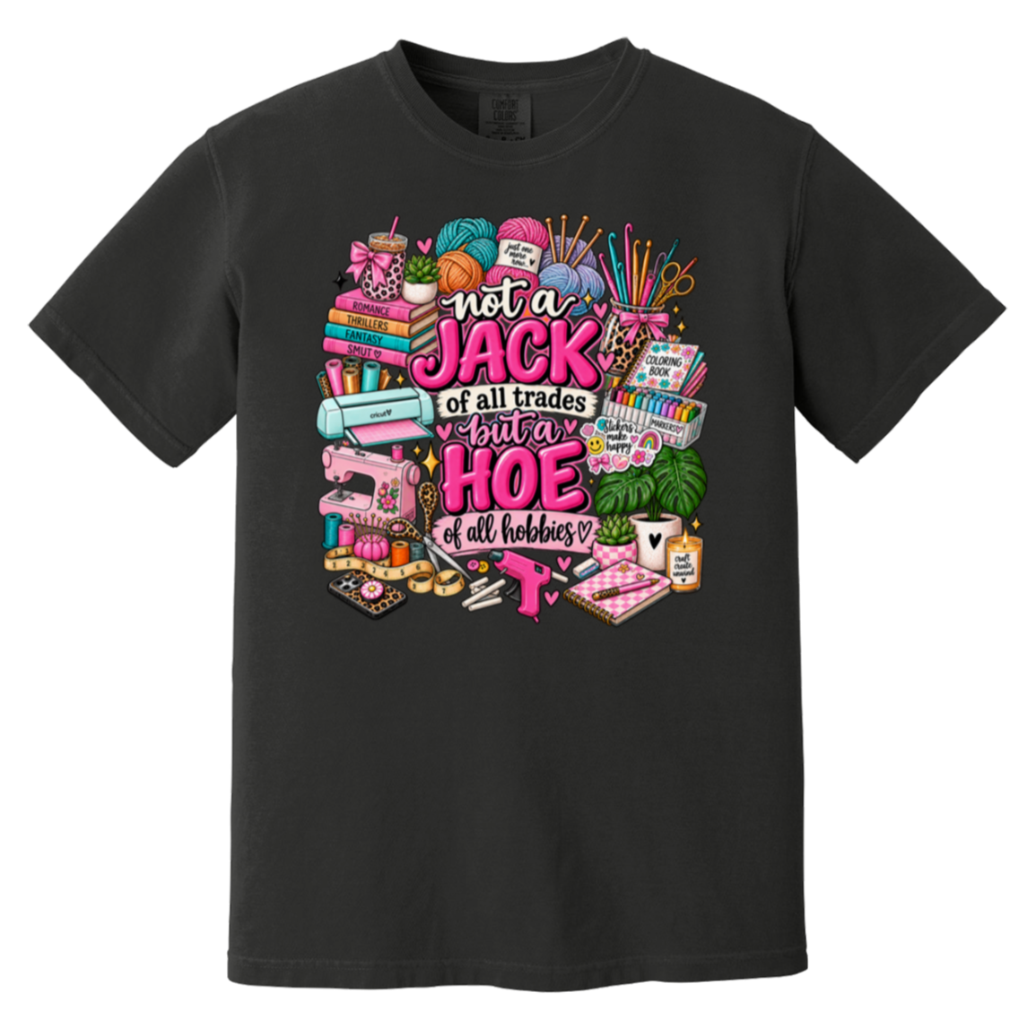 A black short-sleeve crewneck t-shirt featuring a colorful graphic print on the front. The graphic contains various hobby and crafting items like knitting needles, yarn, a sewing machine, and tools, surrounding the text 'not a JACK of all trades but a HOE of all hobbies' in pink and white lettering.