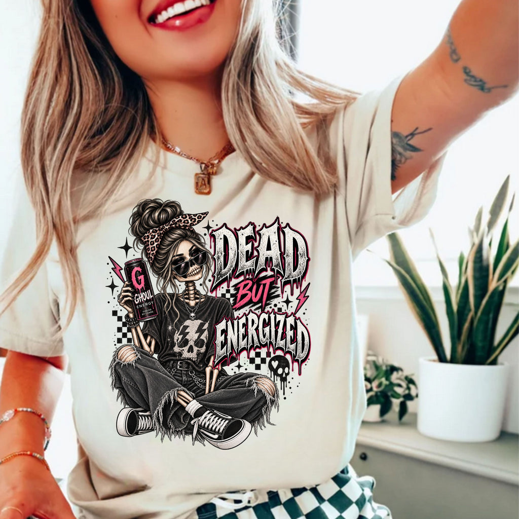 a woman wearing a white tshirt with the graphic of a skeleton wearing jeans and a tshirt holding an energy drink with a text "DEAD BUT ENERGIZED"