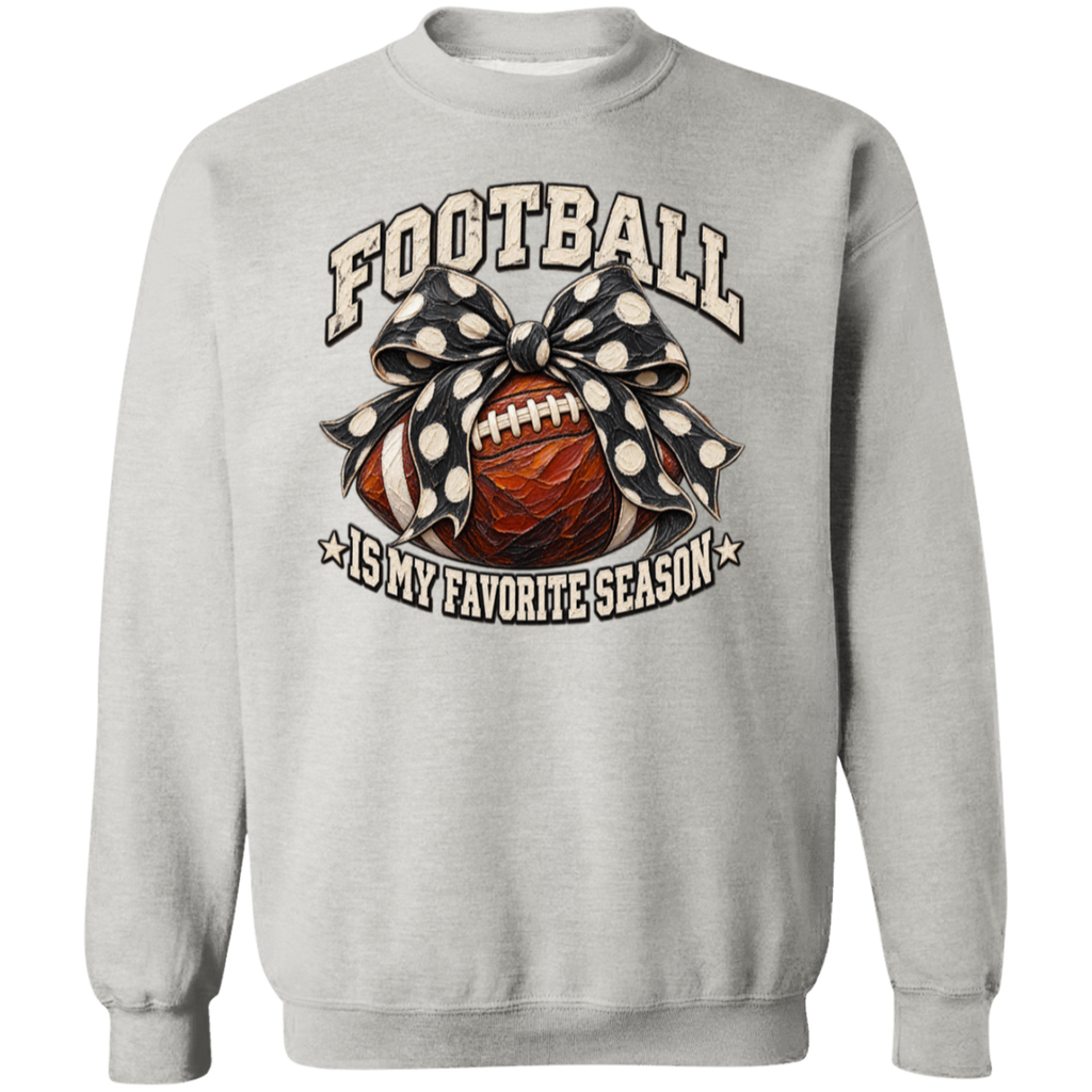 A light gray crewneck sweatshirt featuring a graphic design on the front with the text 'FOOTBALL IS MY FAVORITE SEASON'. The graphic depicts a brown football wrapped in a black and white polka dot bow, set against a clean white background.