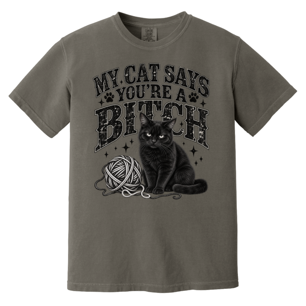 A short-sleeve crewneck t-shirt in a muted grayish-brown color, featuring a black graphic print of a cat sitting next to a ball of yarn with the text 'MY CAT SAYS YOU'RE A BITCH' in a distressed font.