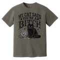A short-sleeve crewneck t-shirt in a muted grayish-brown color, featuring a black graphic print of a cat sitting next to a ball of yarn with the text 'MY CAT SAYS YOU'RE A BITCH' in a distressed font.