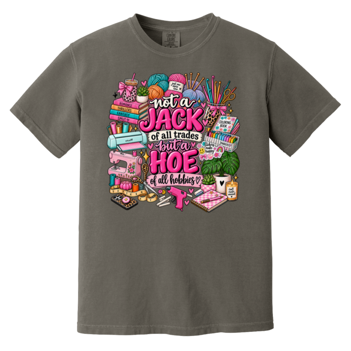A dark gray crewneck t-shirt featuring a colorful graphic print on the front. The graphic displays various sewing and crafting tools, yarn, and books arranged around the text 'not a JACK of all trades super HOE of all hobbies', with a pink sewing machine and sewing needle in the center.