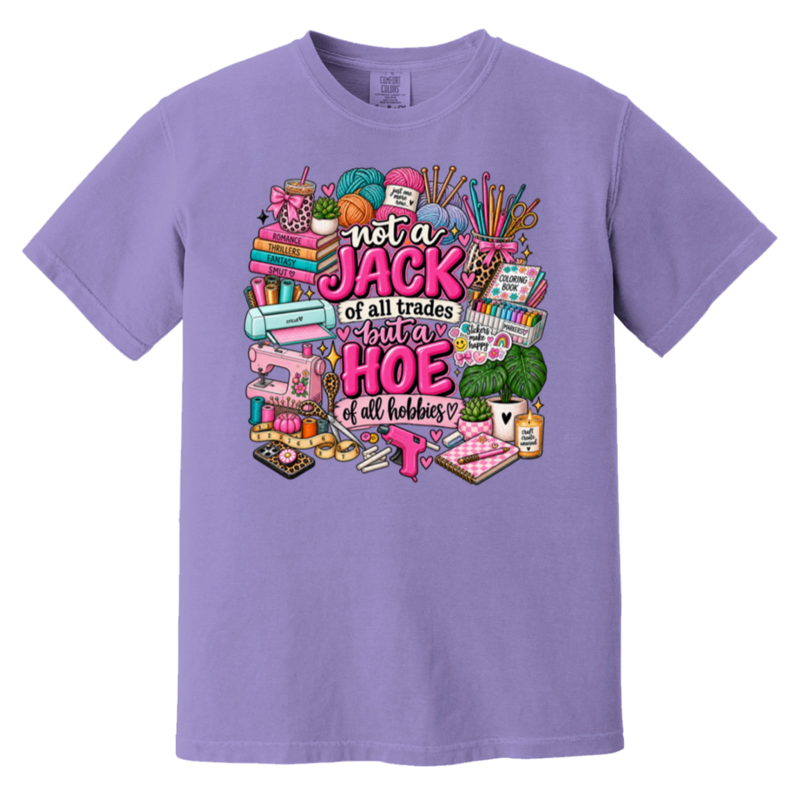 A lavender purple short-sleeve crewneck t-shirt featuring a colorful graphic print on the front. The graphic contains various hand-drawn sewing and crafting tools (sewing machine, yarn, scissors, thread) surrounding the text 'not a JACK of all trades but a HOE of all hobbies' in pink and white lettering.