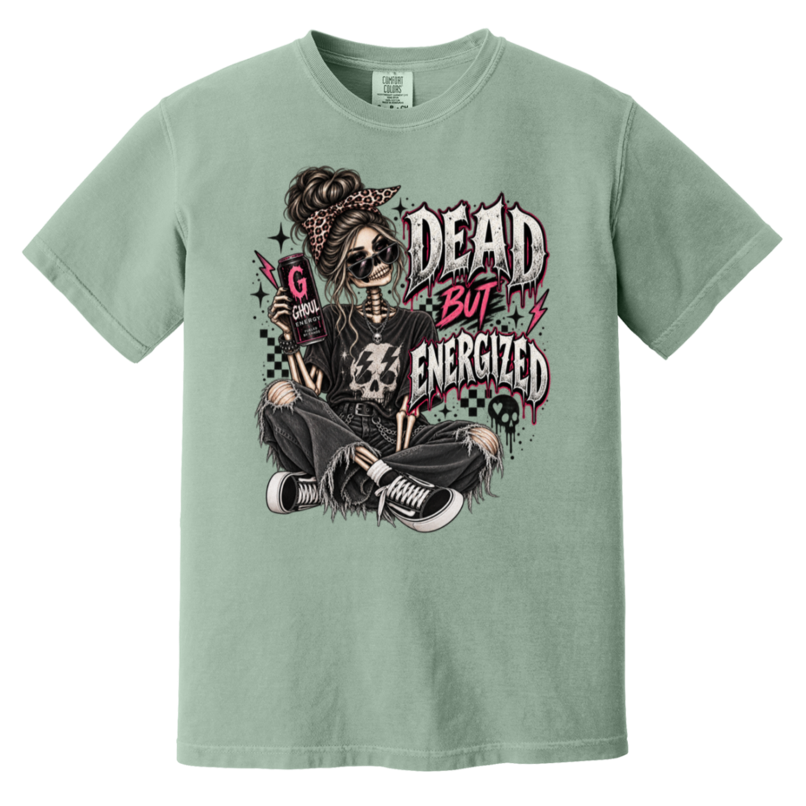 A sage green short-sleeve t-shirt with a detailed graphic print on the front. The graphic features a skeleton woman with sunglasses, a bandana, and a skull, sitting cross-legged next to the text 'DEAD BUT ENERGIZED' in a distressed, graffiti-style font.