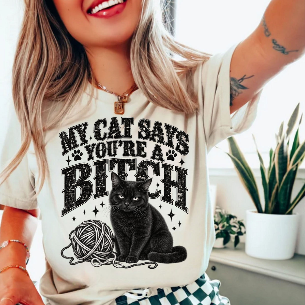 a woman wearing a white tshirt with the text "my cat says you're a bitch" and a graphic of a black cat with a ball of yarn
