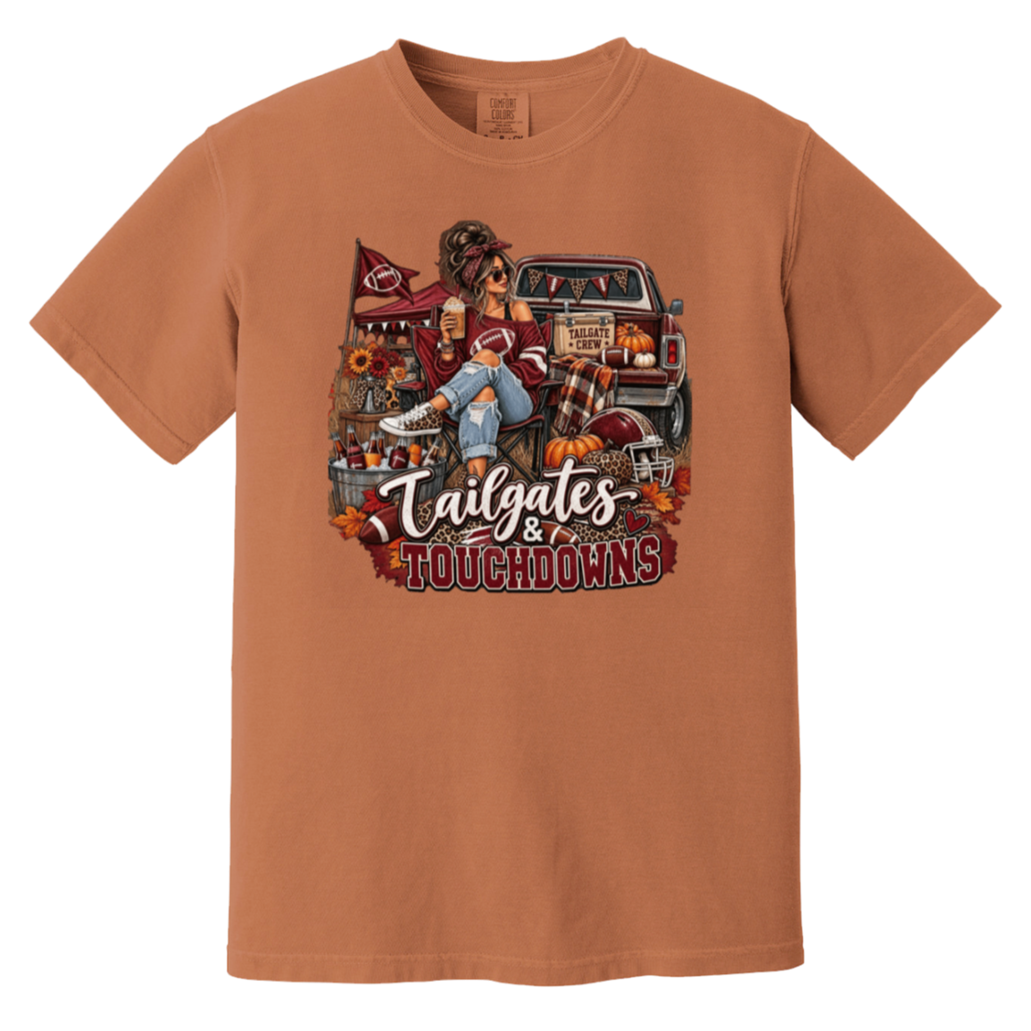 Rust orange  graphic T-shirt with a detailed autumn football scene printed on the front, including a truck, pumpkins, sunflowers, and the text 'Tailgates & Touchdowns'.