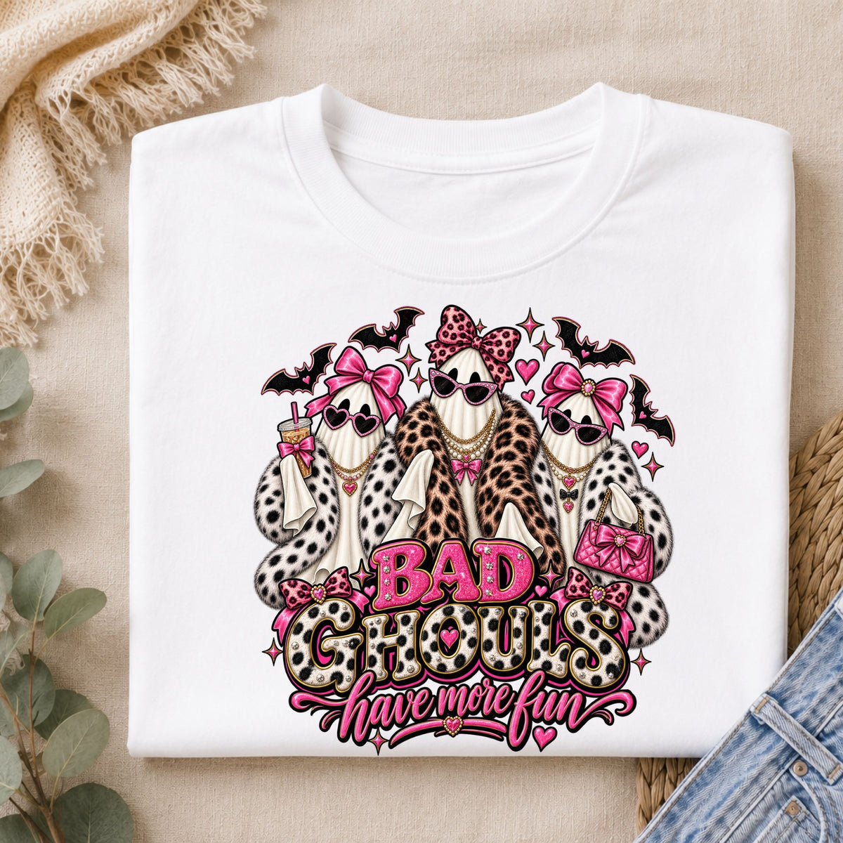 white t-shirt with a graphic print of three ghosts dressed in faux fur outfits and pink bows, with the text 'BAD GHOULS have more fun' in pink and leopard print.