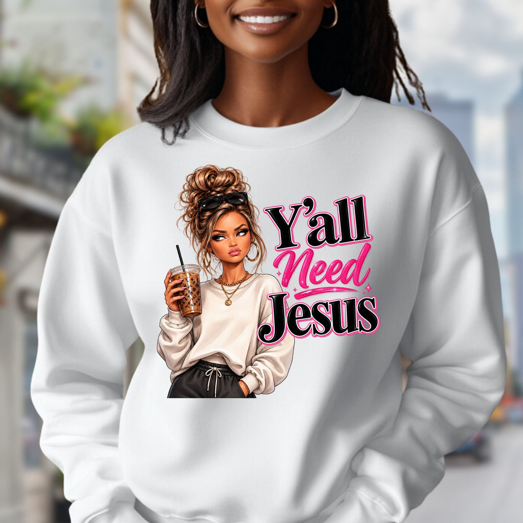 A woman wearing a white crewneck sweatshirt with a graphic print of a woman holding an iced coffee next to the text 'Y'all Need Jesus' in pink and black. The background is a blurred outdoor street scene.